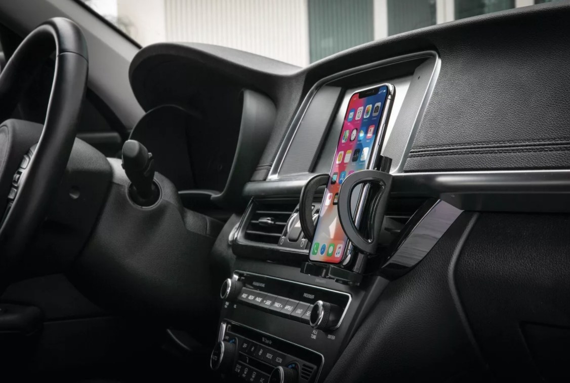 The black mount is holding an unlocked phone against a black dashboard and interior of a car