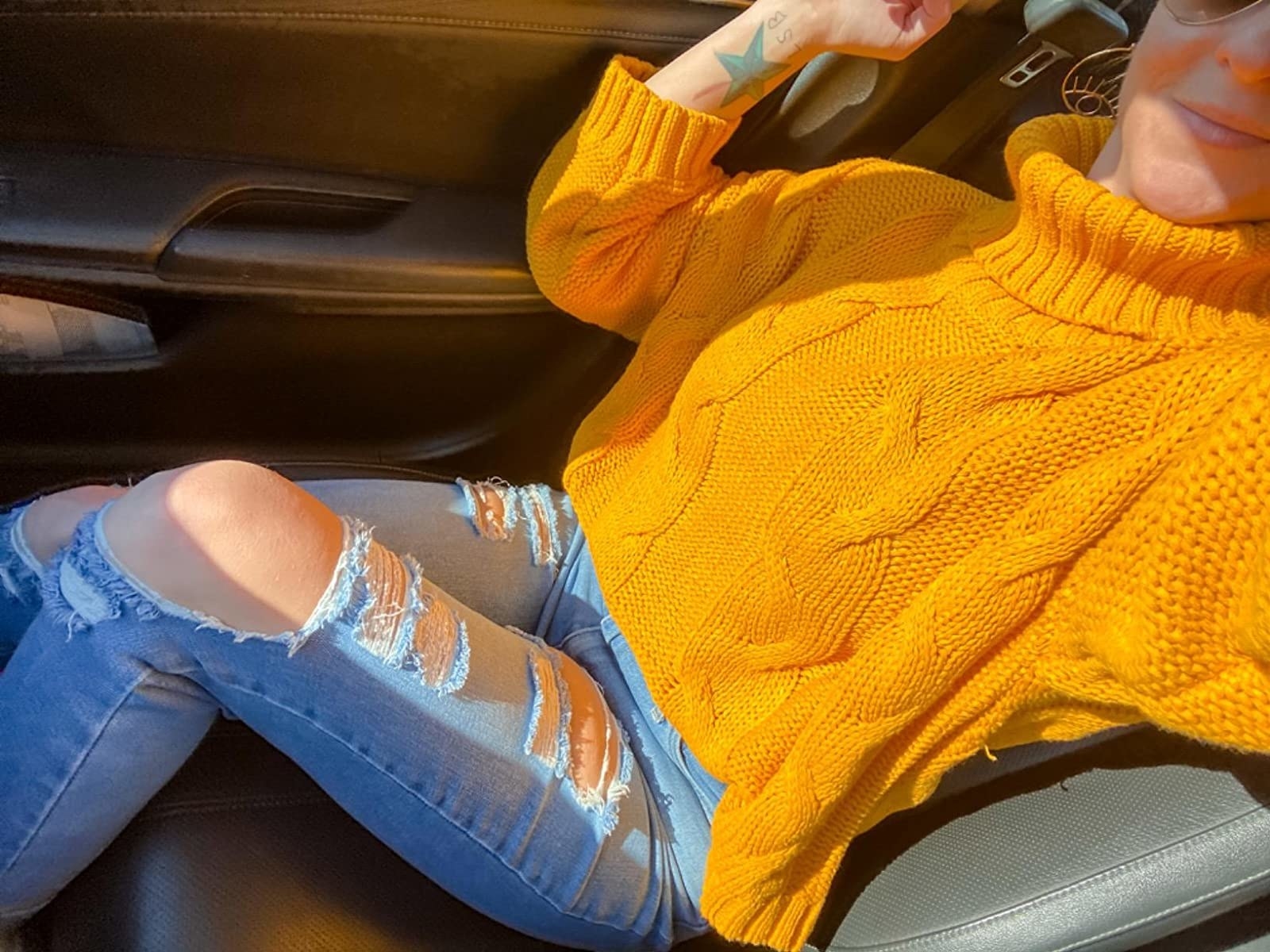 A reviewer wearing the yellow turtleneck sweater with distressed blue jeans