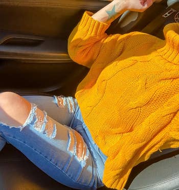 A reviewer wearing the yellow turtleneck sweater with distressed blue jeans