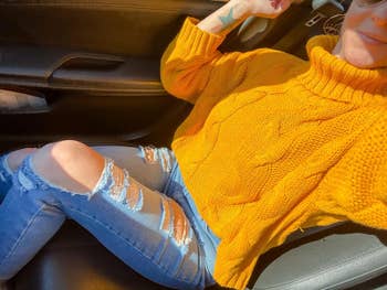A reviewer wearing the yellow turtleneck sweater with distressed blue jeans