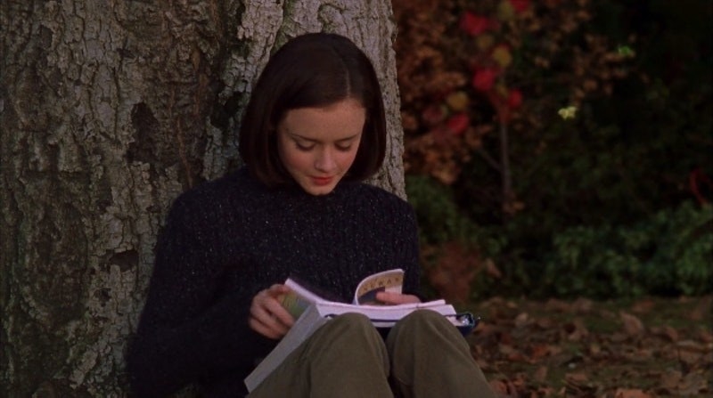 A young woman reading a book under a tree