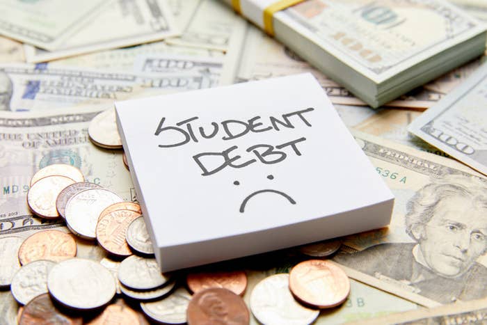 Sticky note with the words &quot;student debt&quot; and a sad face on a pile of money