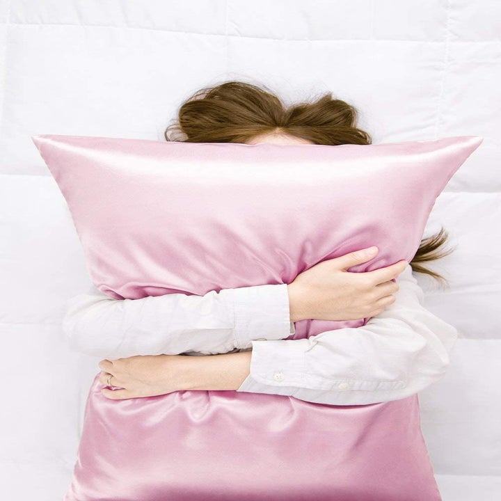 model hugging a pillow with pink satin pillow case on it