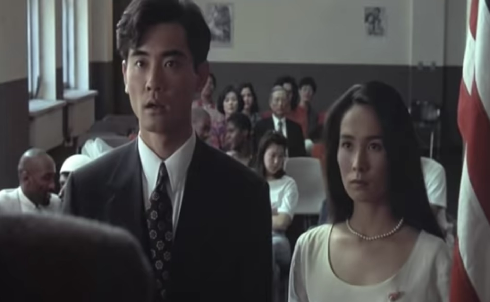 Actors Winston Chao and May Chin stand beside each other in a courtroom looking surprised.