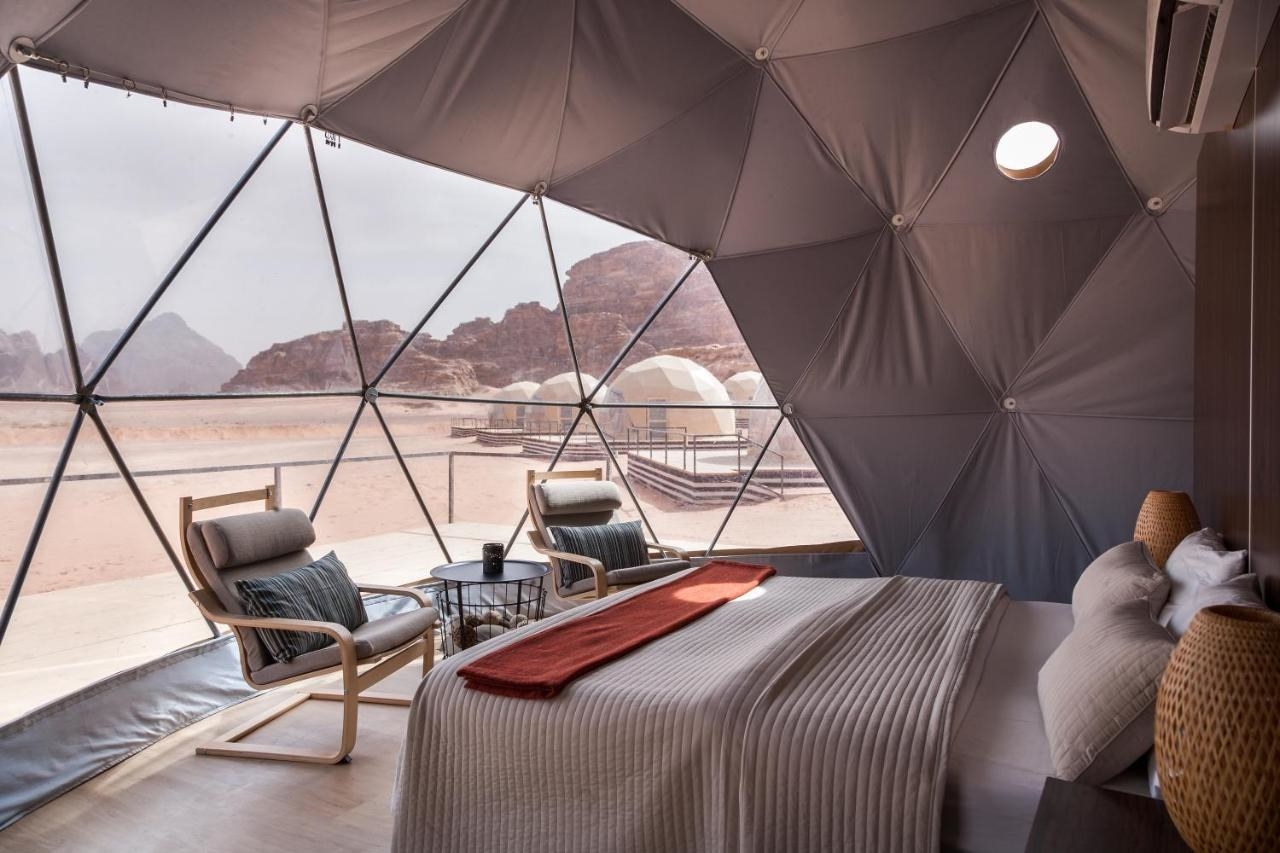 View from inside the martian dome texts with bed and two lounge chairs and large windows looking out at the desert.