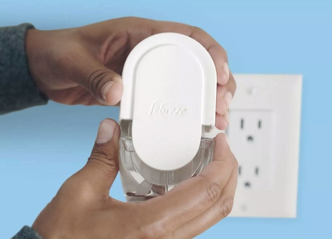 An adult is holding the device that has a white cover that says &quot;febreze&quot; and a clear bottom