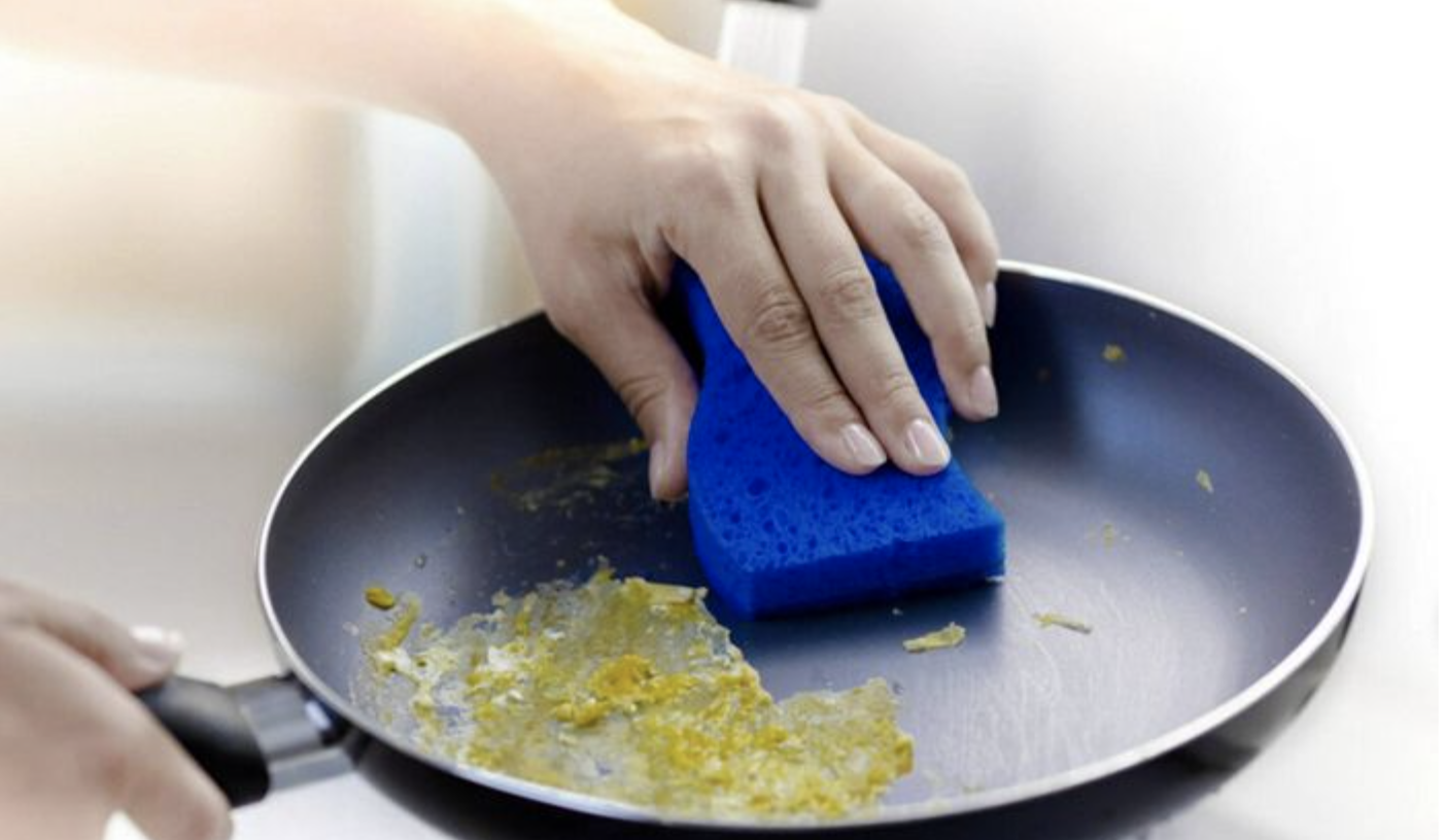 person cleaning stuck on eggs off a fry pan with the sponge