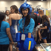 Woman dressed in a blue comic con outfit points at the camera.
