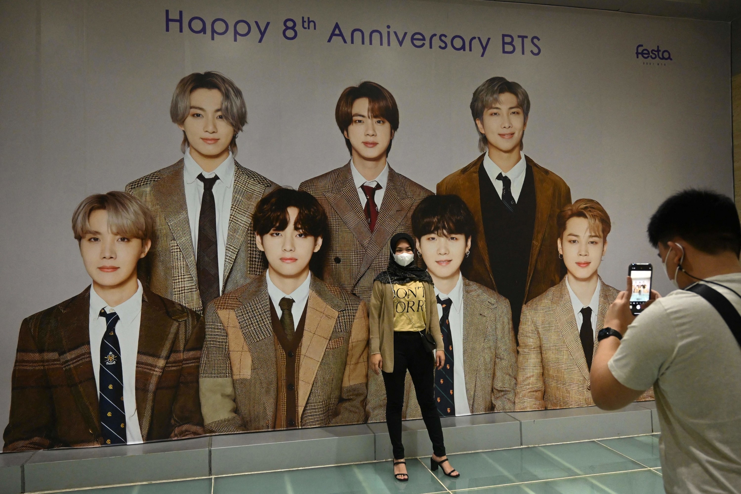 Someone takes a picture of a masked person standing in front of a photo of BTS