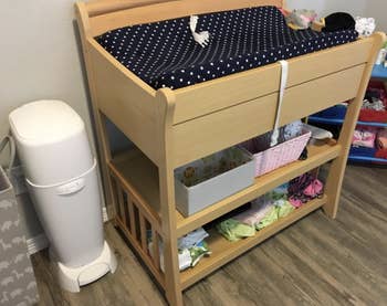 a reviewer photo of the diaper genie next to a changing table