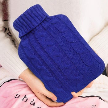 Model holding the hot water bottle in its knit cozy in blue
