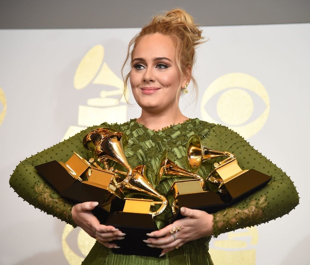 Adele holding five Grammy awards in her arms backstage