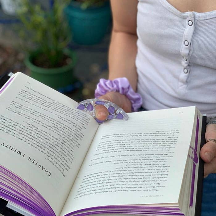 readers wears purple resin book page holder while reading two pages in book