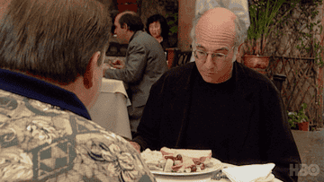 Larry David looking at a plate of food.