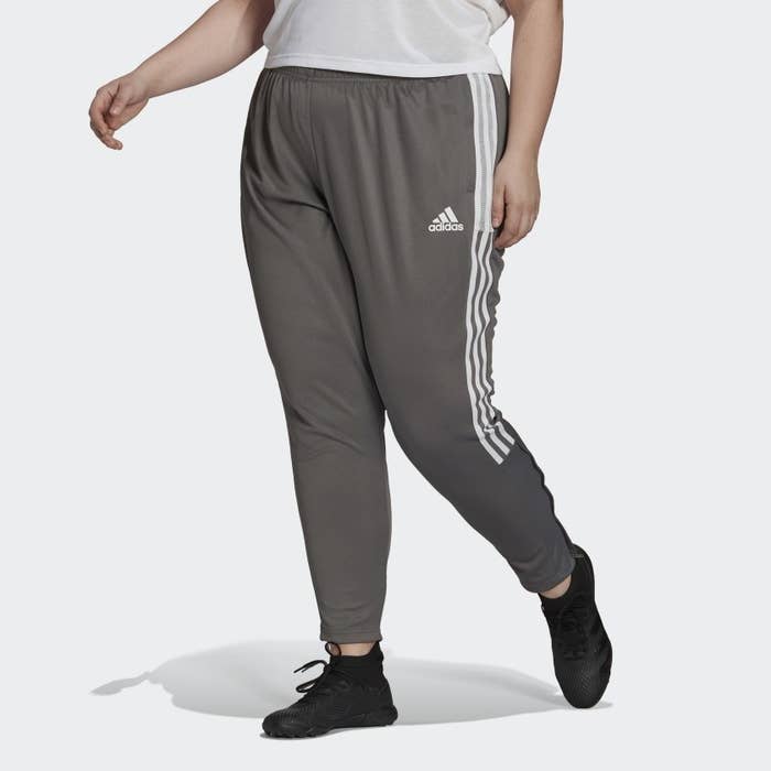 model wears gray, jogger-like track pants with three white stripes on the side