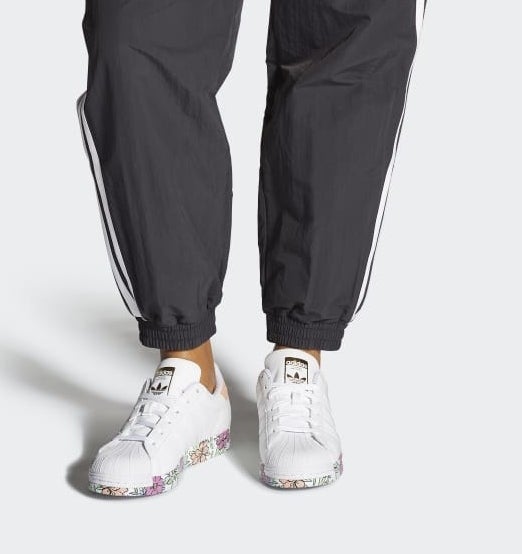 model in white and floral-printed Adidas sneakers and black track pants