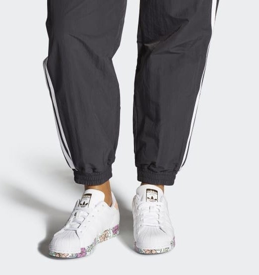 model in white and floral-printed Adidas sneakers and black track pants