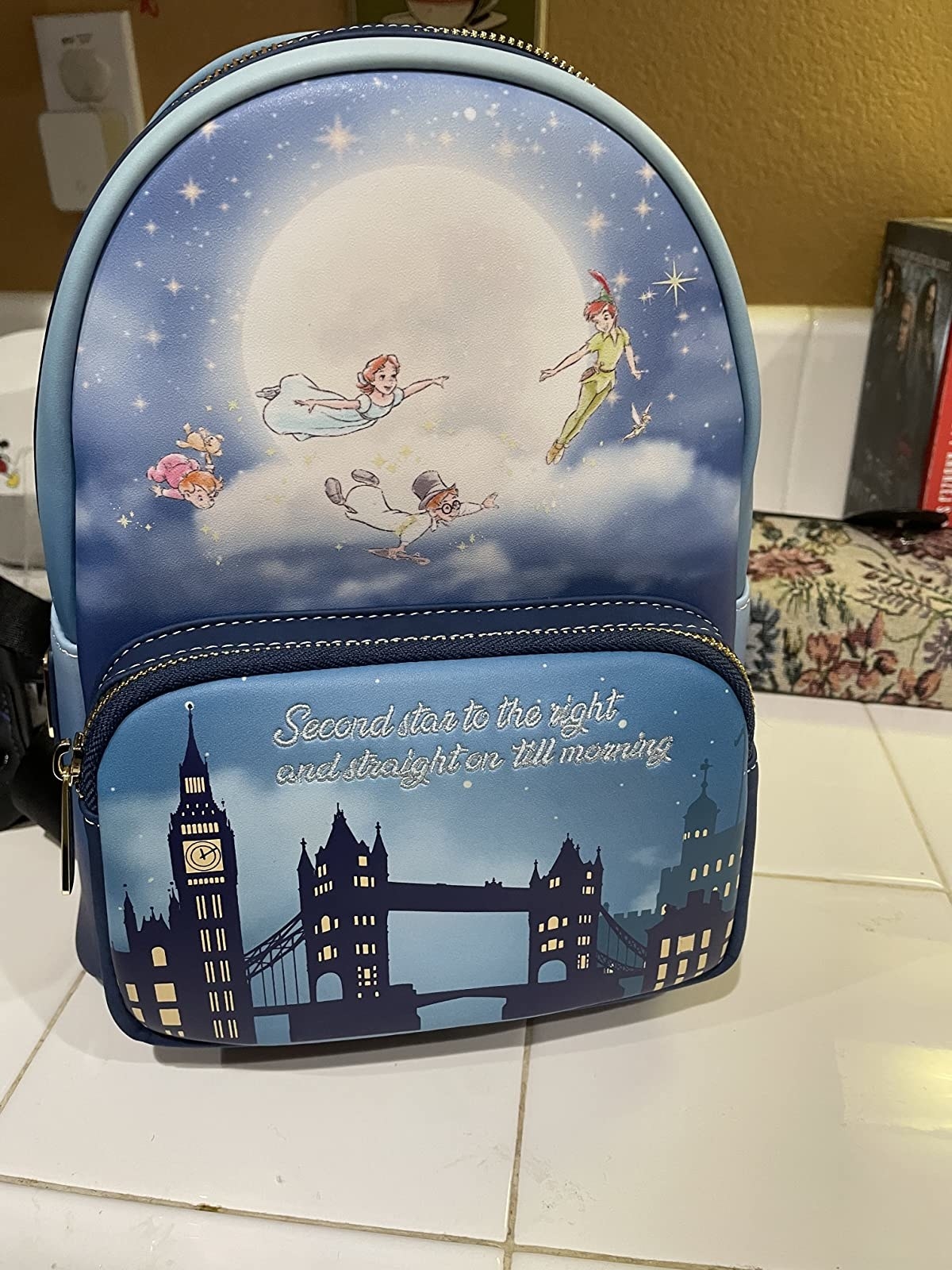 a peter pan backpack with &quot;second star to the right and straight on till morning&quot; embroidered on it and the scene of the kids flying over the bridge