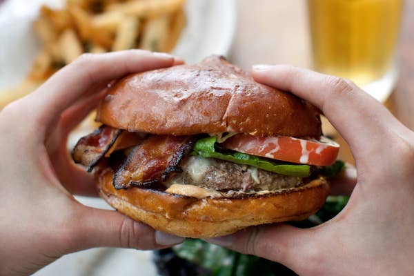 Holding a bacon cheeseburger.