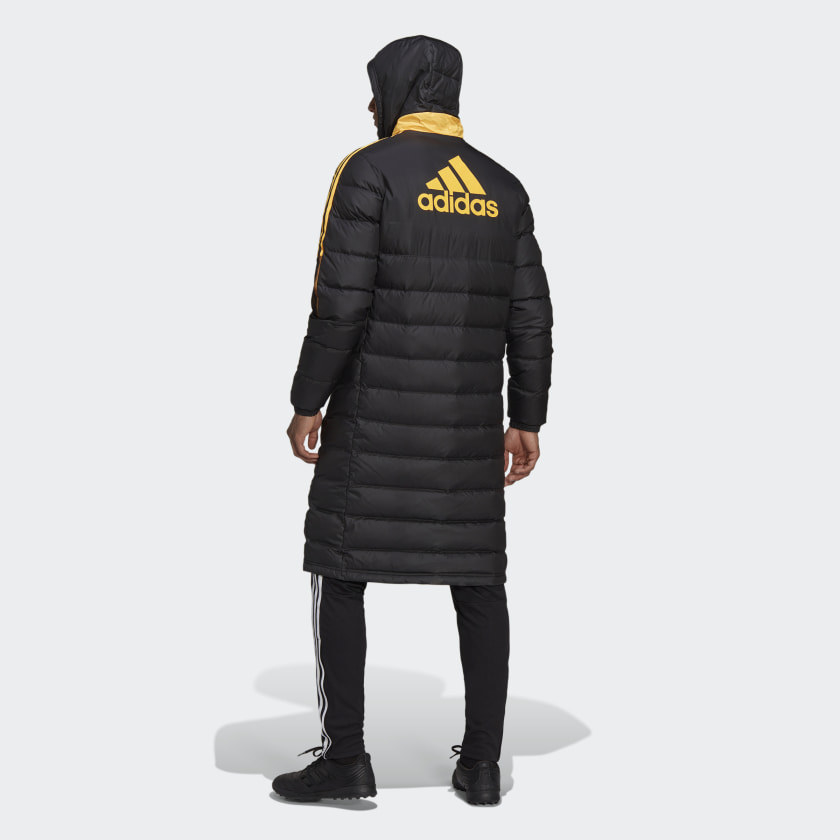 Model shown from behind wearing the black coat with yellow Adidas logo and three stripes going down the sleeves