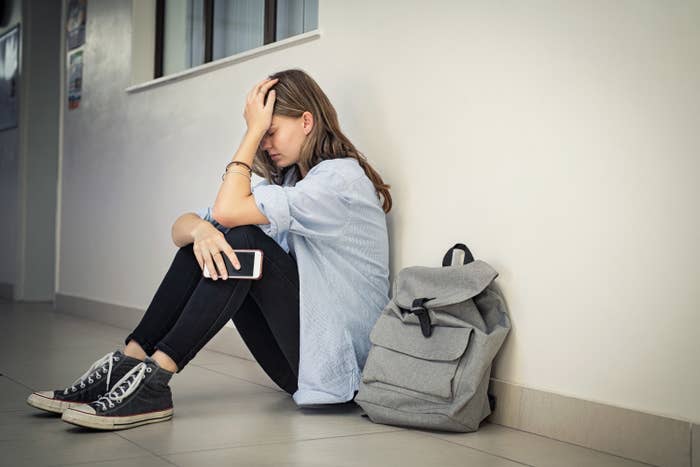 A girl sitting on the floor with her head to her hand looking sad
