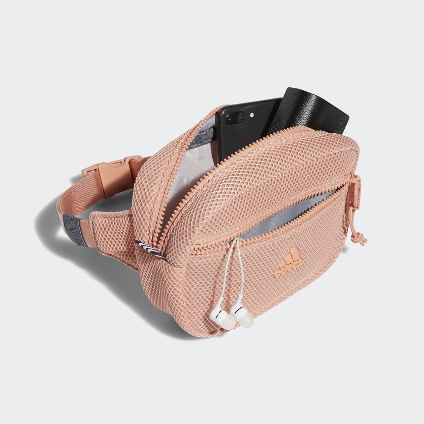 light pink mesh waist pack with two pockets filled with earbuds and a smartphone and wallet