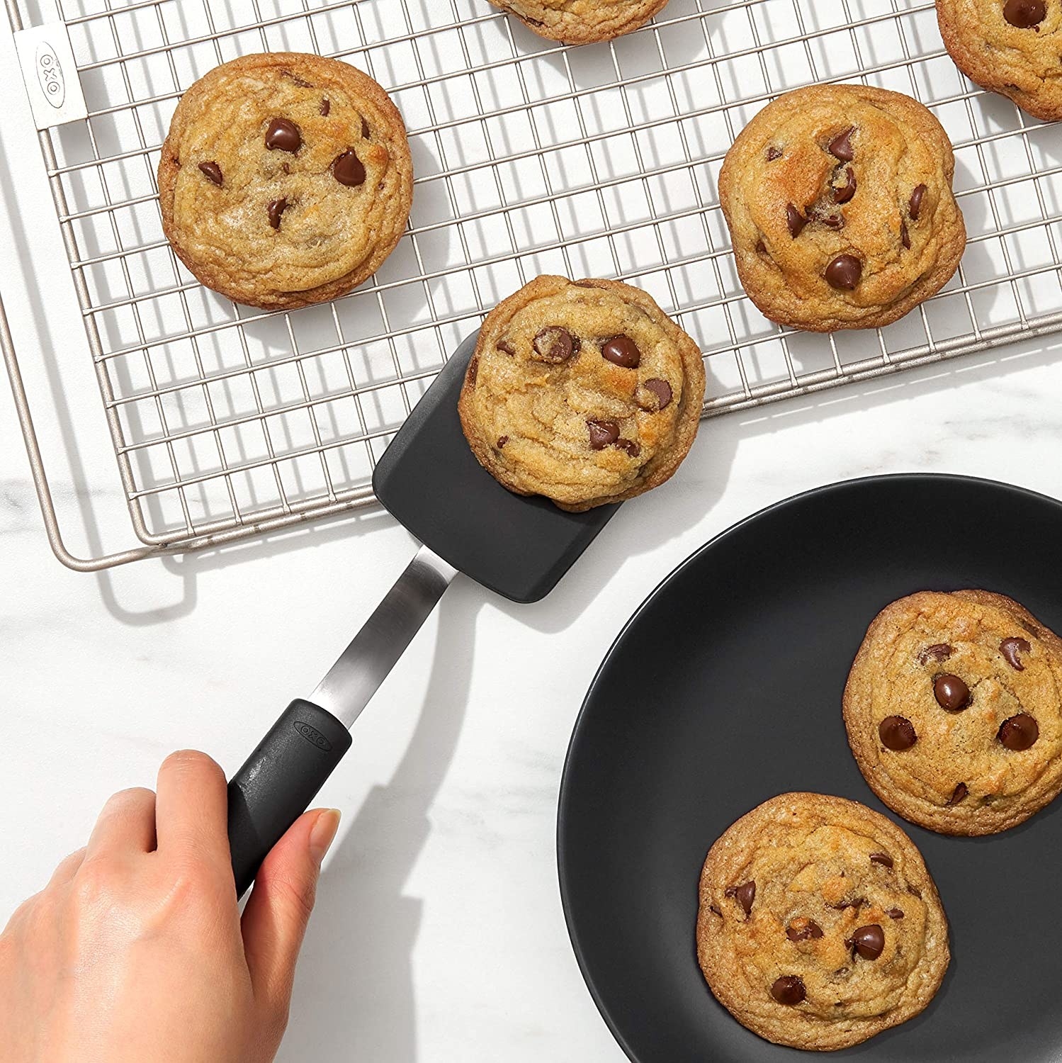 Model&#x27;s hand using the spatula to lift cookies from a cooling rack