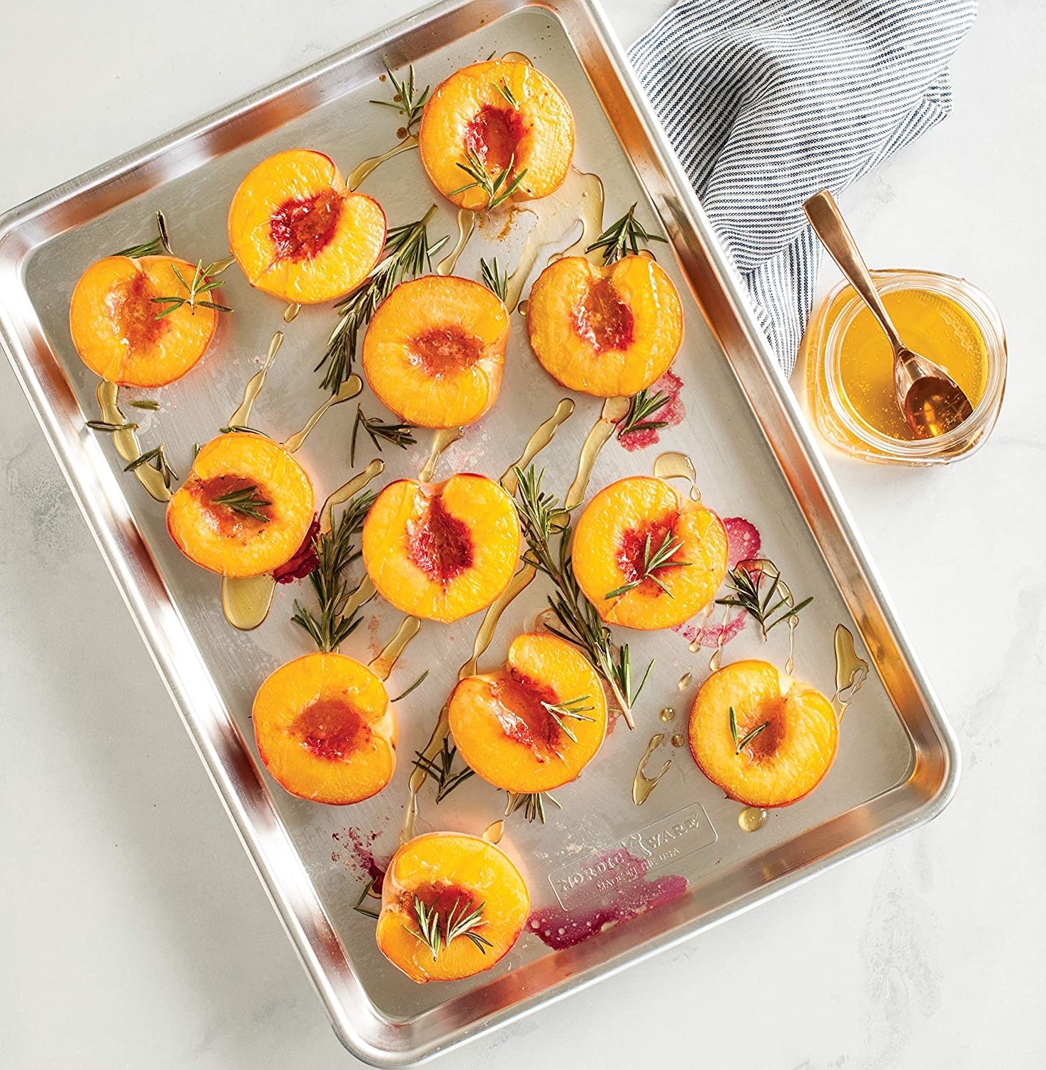 Halved peaches and rosemary sprigs on the sheet tray
