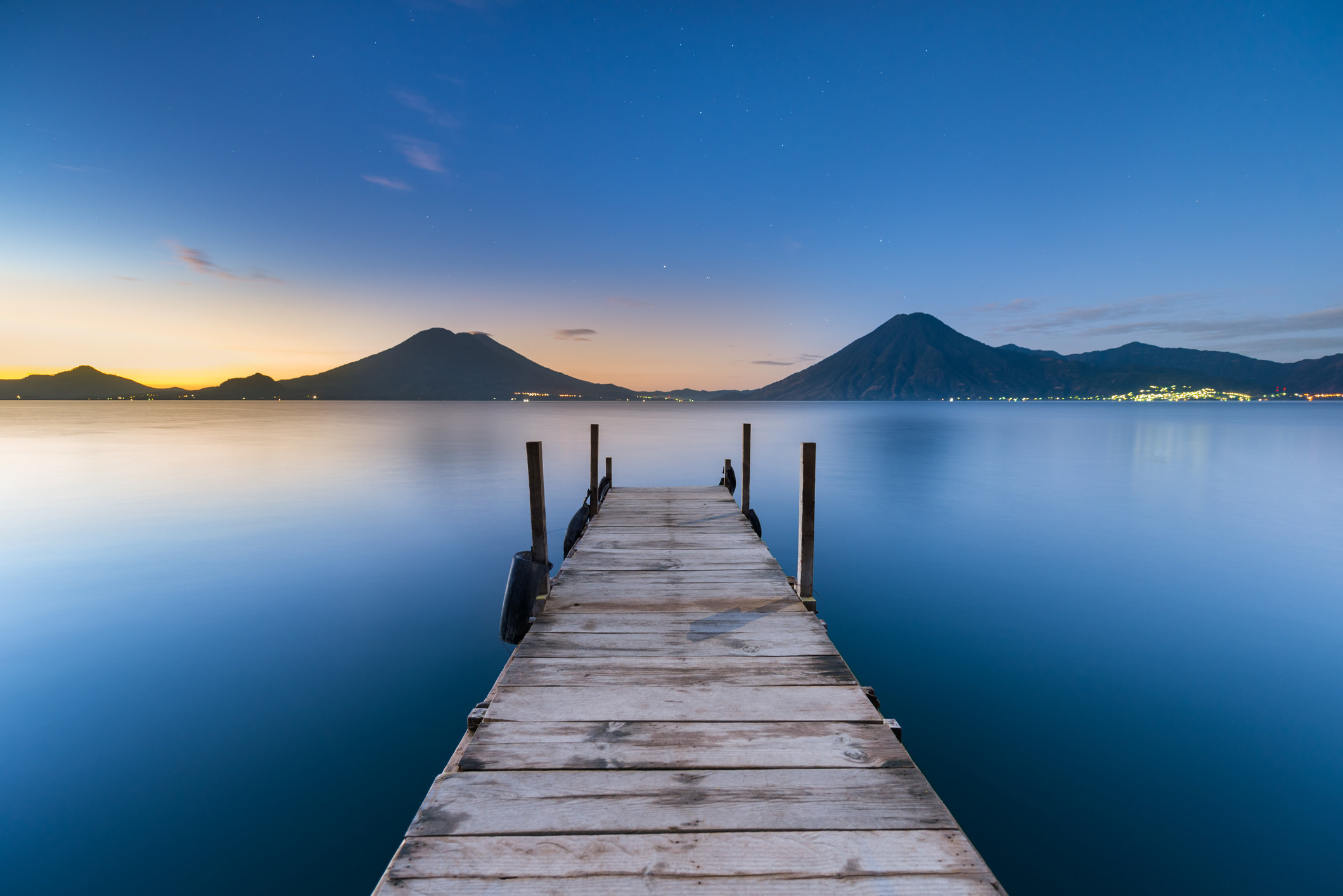 A dock into calm lake with volcanoes in the distance