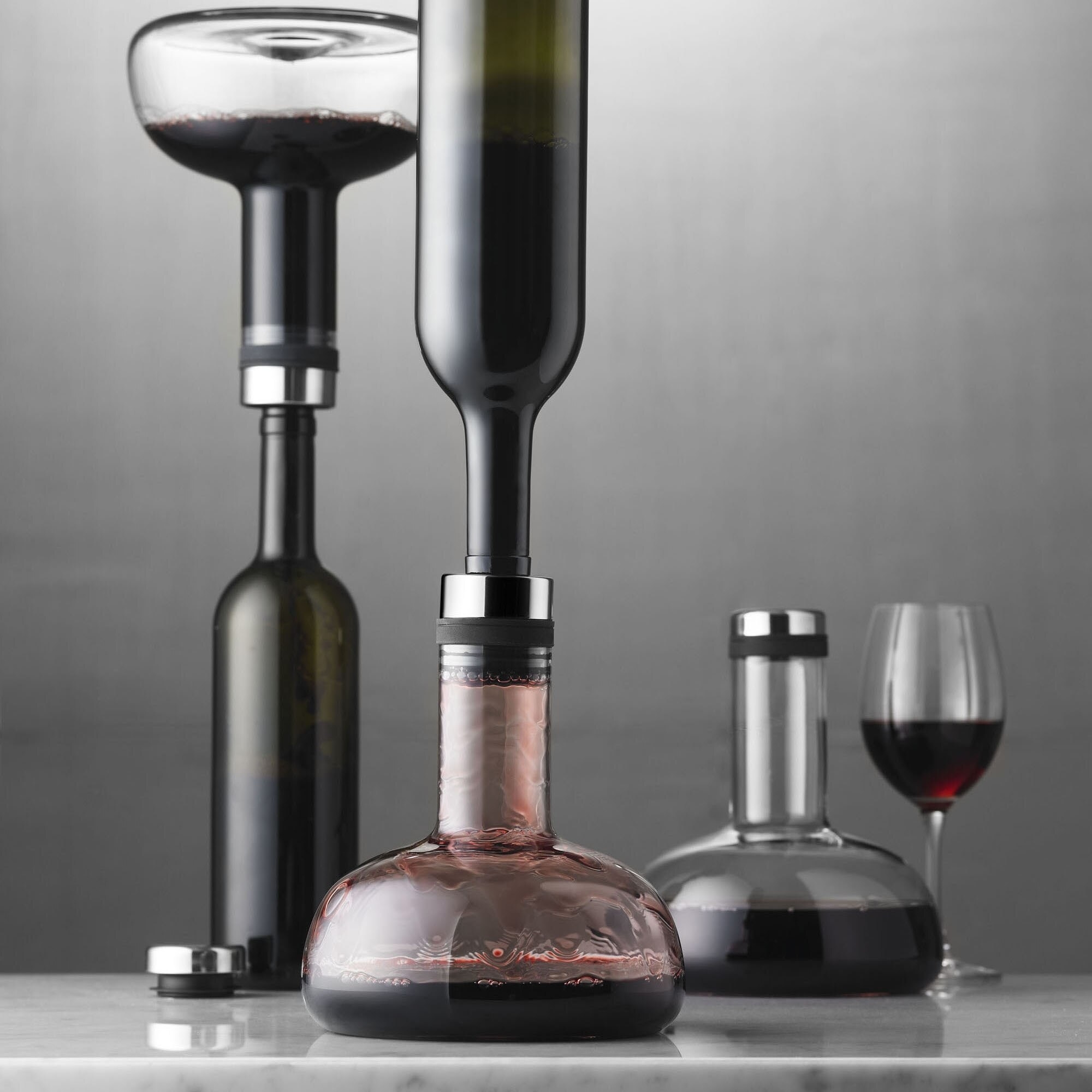 a trio of aerating carafes aerating several bottles of red wine