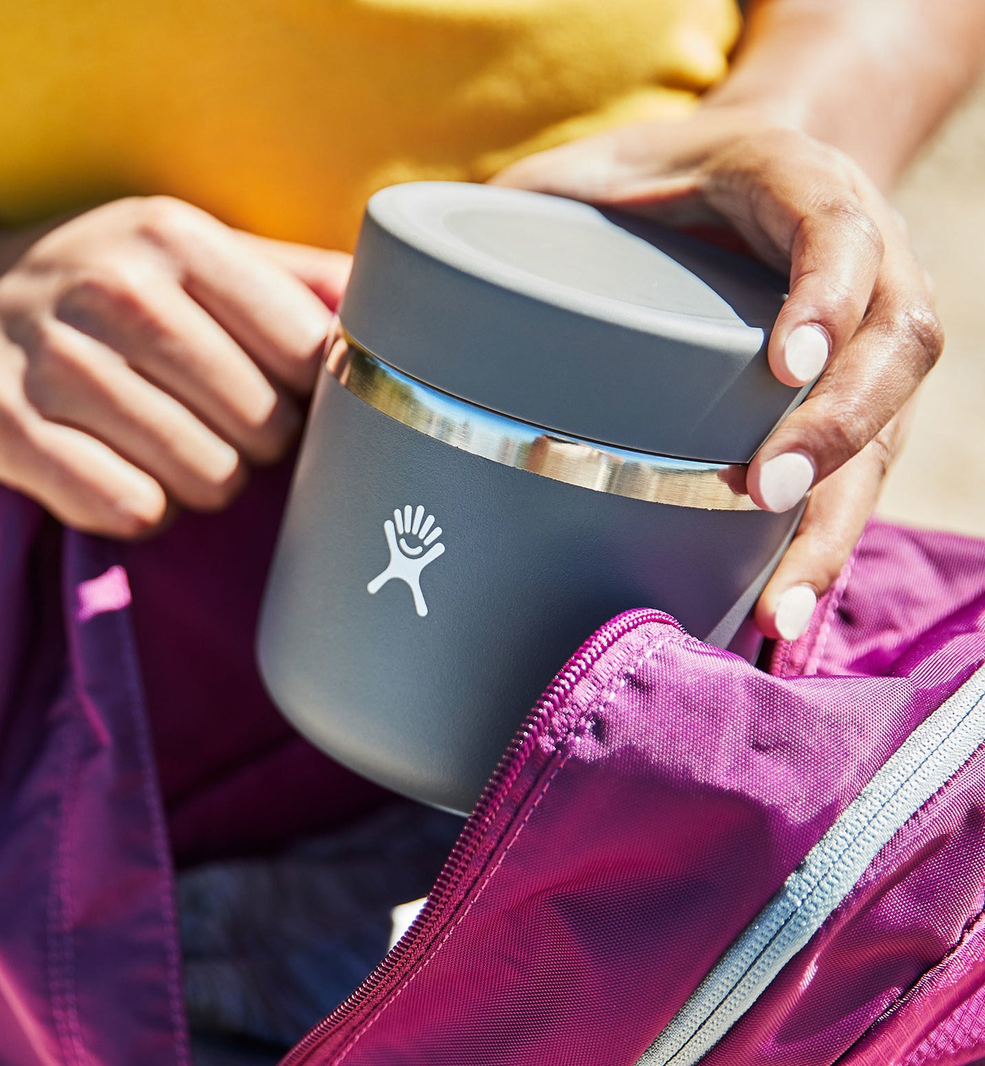 model putting grey stainless steel and screw-top food jar into a backpack