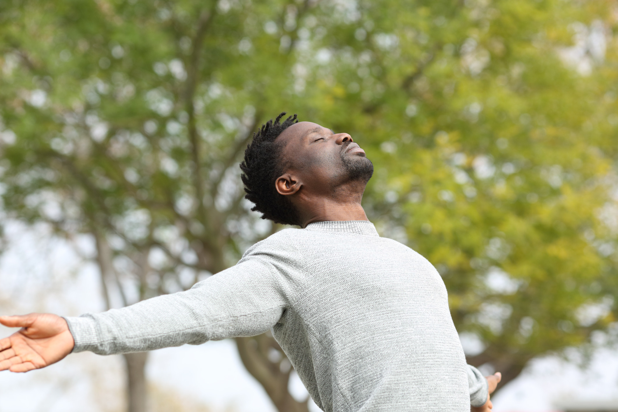 A man stands in a park, breathing deeply while stretching.