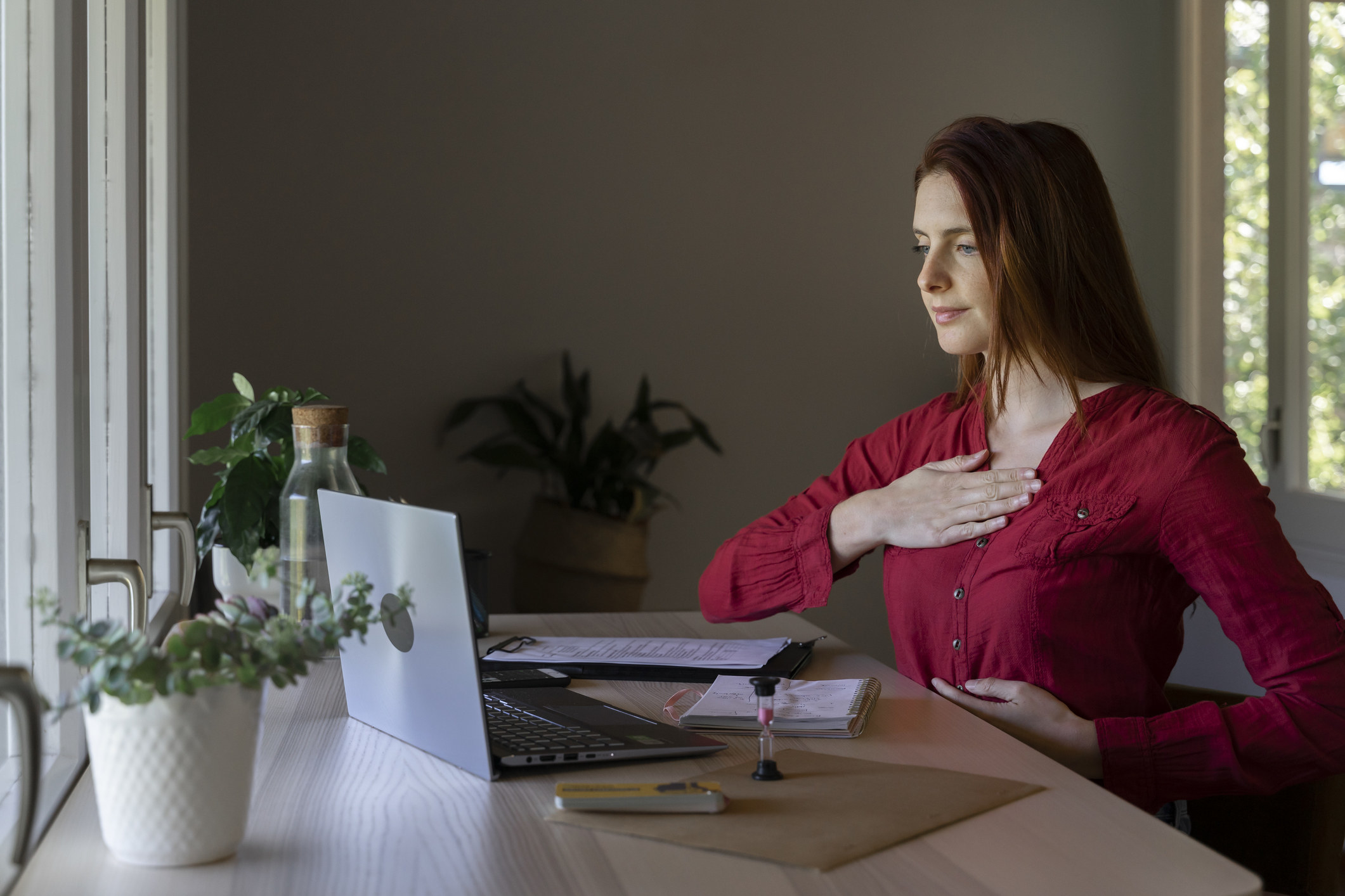 A woman, sitting at her computer, practices breathing exercises.