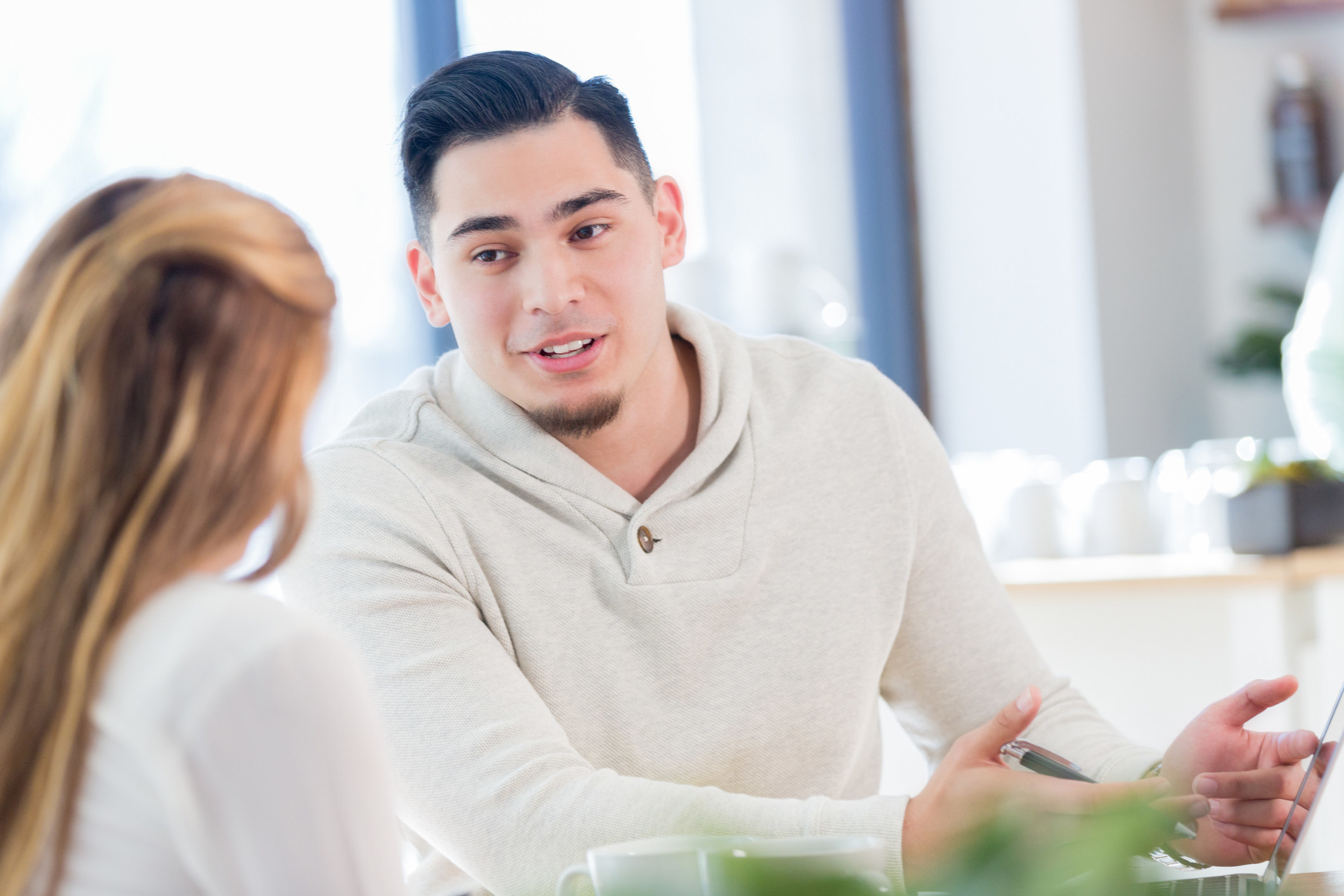 Two students sit at a table talking to each other.