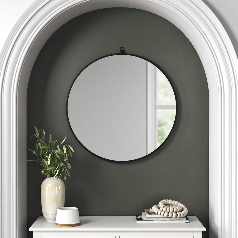 Black framed round mirror above white console table