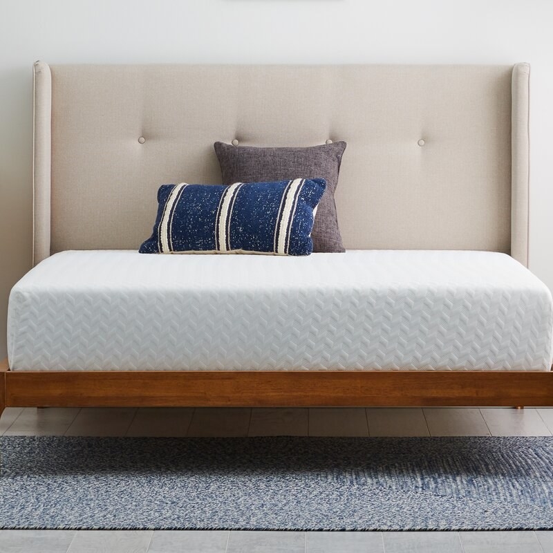 White gel memory foam mattress on wooden bed frame with beige headboard, blue and gray pillow on top