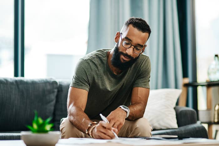 A man sits on his couch, writing a list.