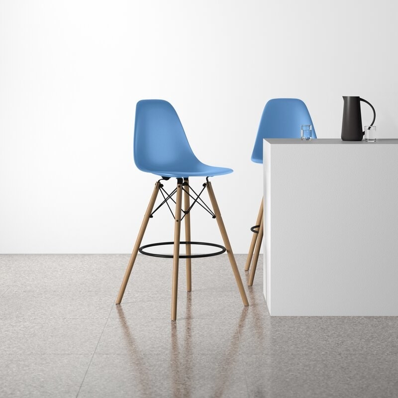 Two blue bar stools with light wooden flared legs around white table