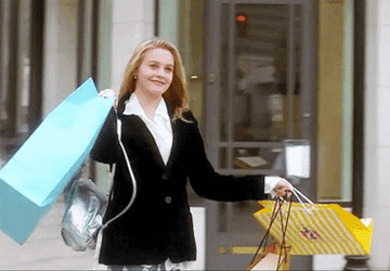 Cher from Clueless smiling while holding shopping bags