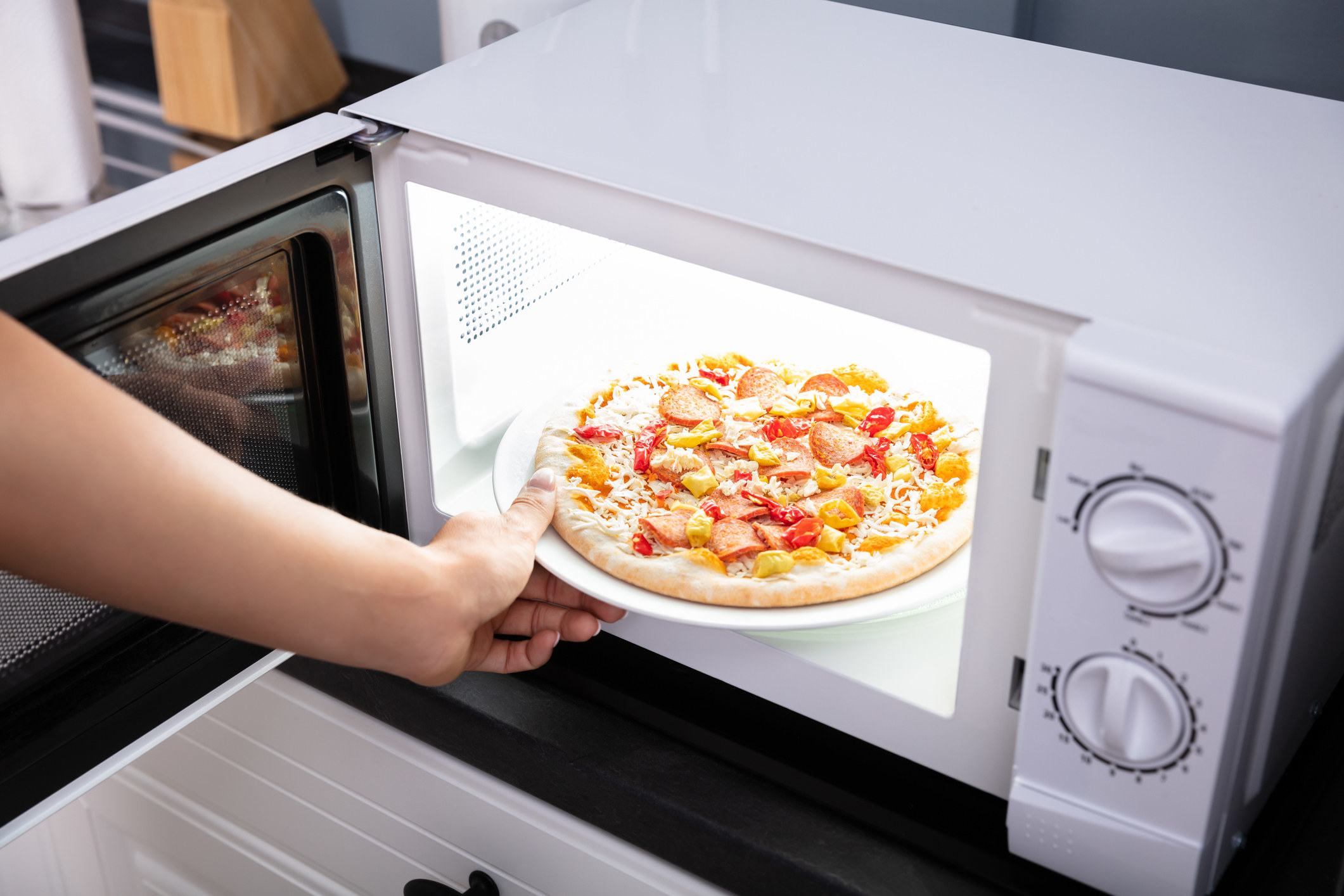 A person putting a pizza in the microwave.