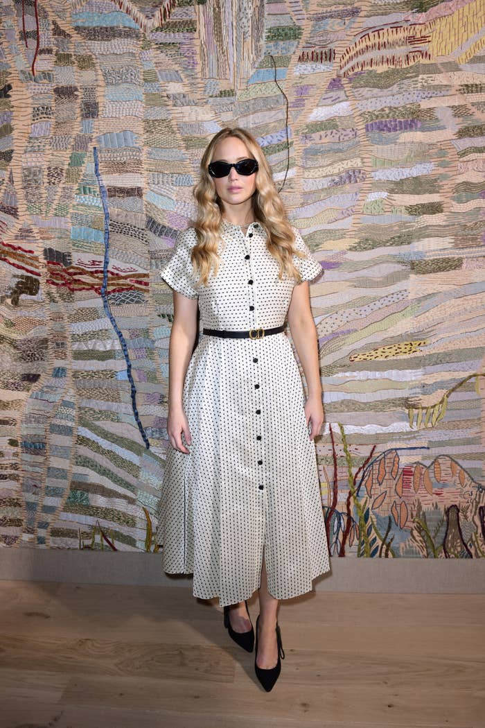 Lawrence wears sunglasses and a ankle-length dress while posing in front of a mural