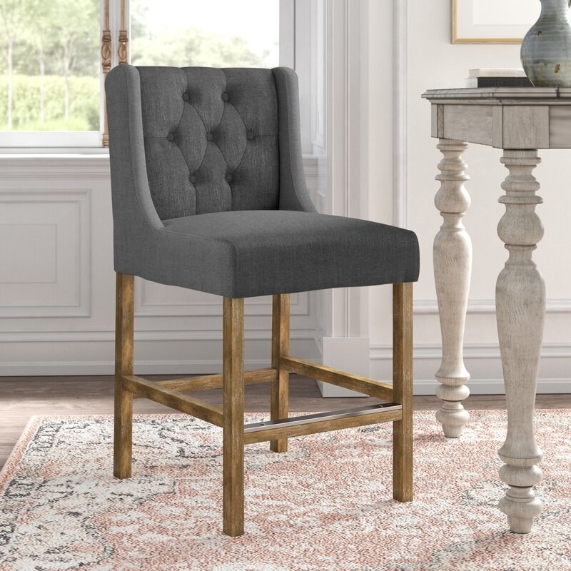 Gray upholstered cushioned bar stool with wooden legs