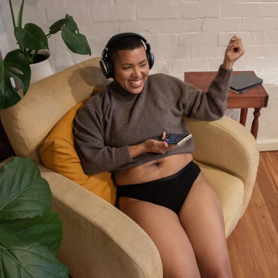 a person wearing headphones and sitting in a comfy chair wearing a sweater and modibodi undies