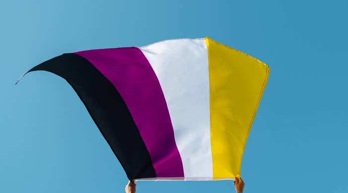 closeup of a young person, seen from behind, waving a non-binary pride flag on the air