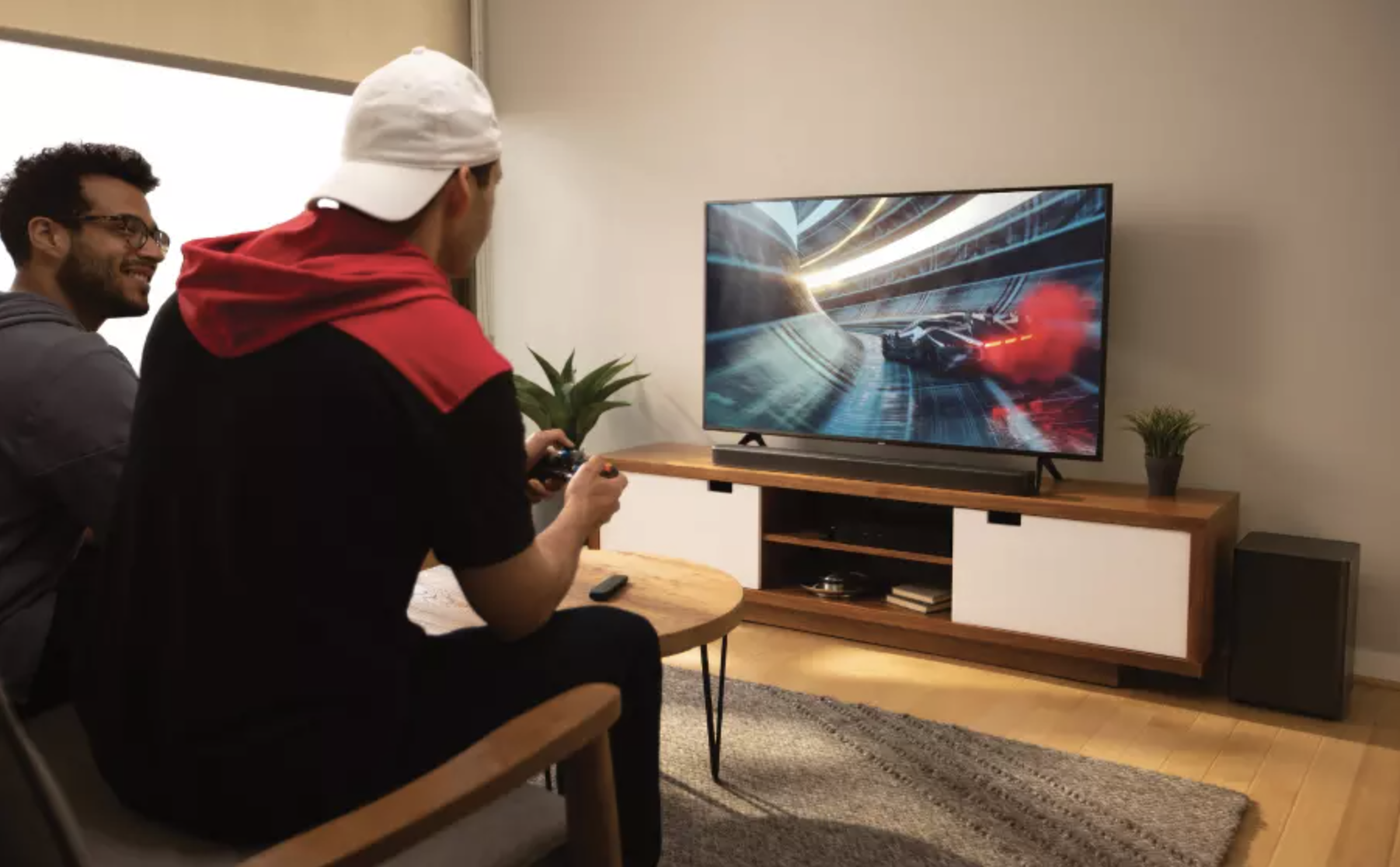 Two people playing video games on a TV connected to the subwoofer and sound bar