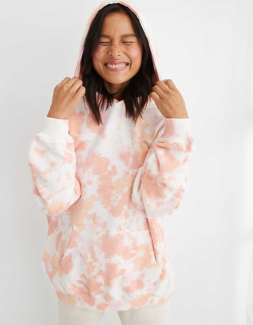 model wearing the hooded sweatshirt with pink and orange tie-dye pattern to it
