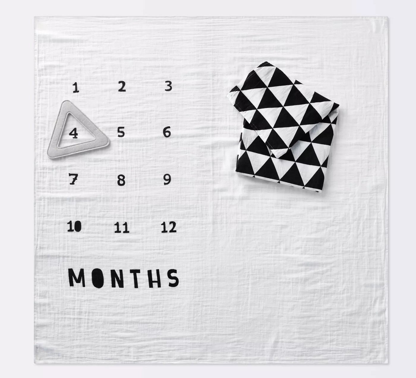 a white muslin blanket that says &quot;months&quot; with the numbers 1 through 12 on it with a triangle frame over the number four and a black and white blanket folded on top