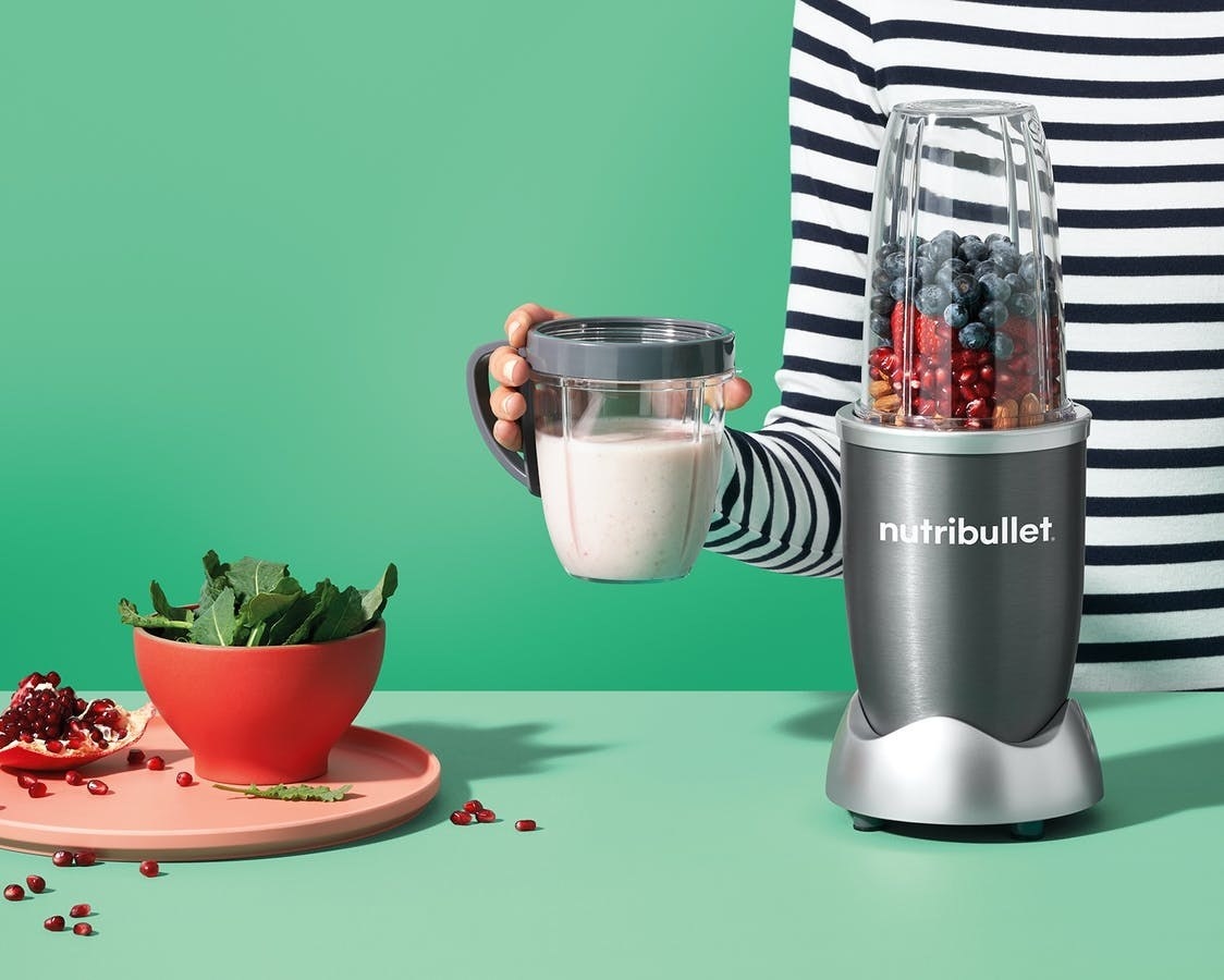 the silver NutriBullet blender next to hand holding smoothie in glass container