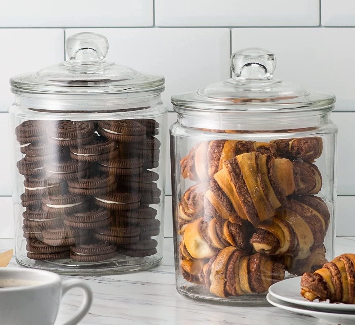 The glass cookie jars on a counter holding cookies and pastries