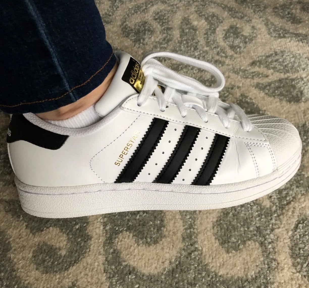 A reviewer wearing the Adidas Originals Superstar sneaker in white with black accents